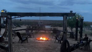 Ein Patio im Freien mit Feuerstelle, Holzstühlen und einer Pergola.