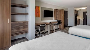 Une chambre d’hôtel avec deux lits, un bureau avec une chaise, une télévision et une armoire.
