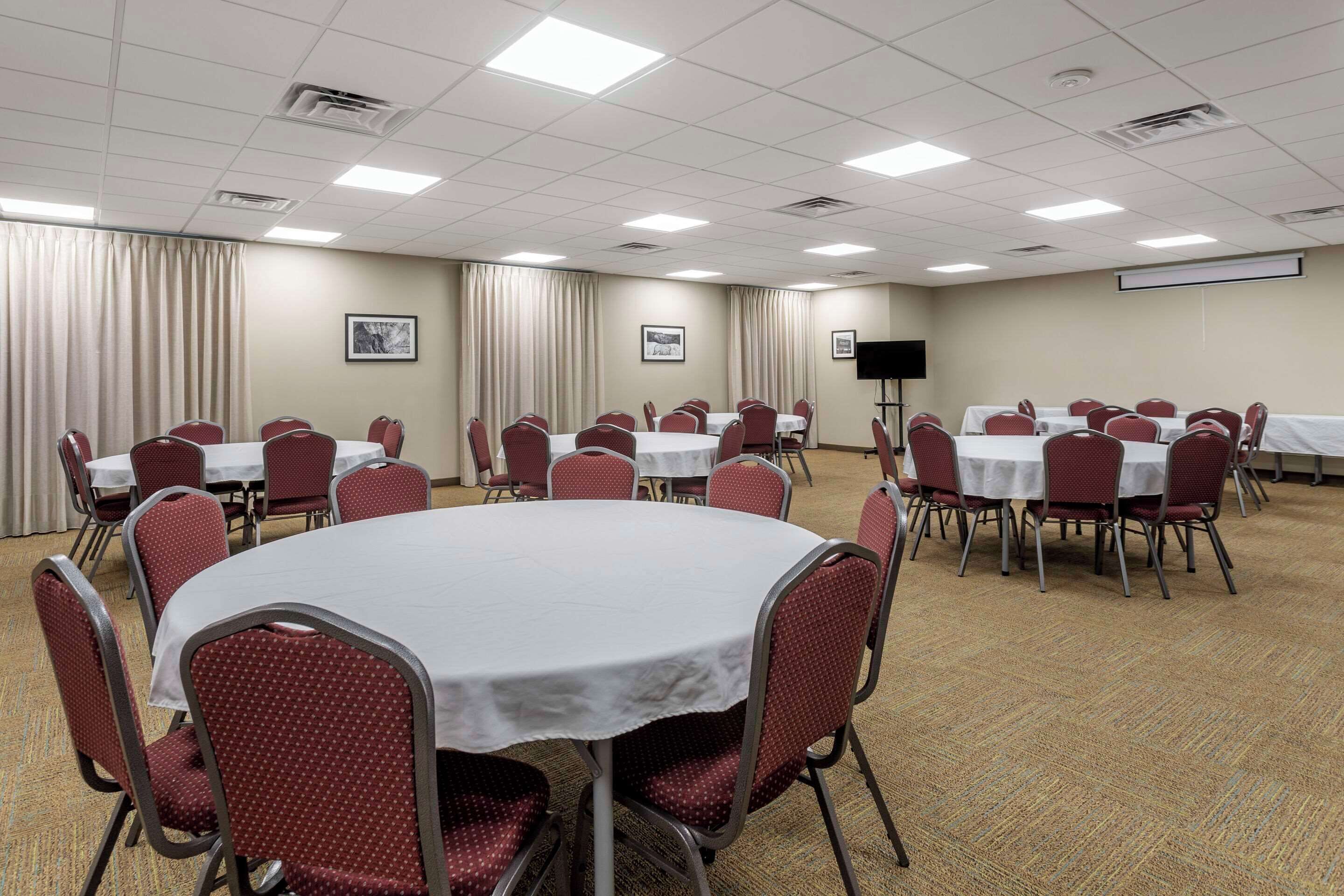 A conference room with multiple round tables, red chairs, and a projector screen.