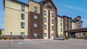Un hôtel moderne à la façade en pierre, avec plusieurs étages et un parking comprenant des places réservées aux personnes handicapées.