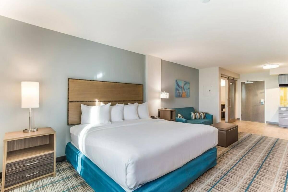 Quarto de hotel com uma cama grande, mesa de cabeceira, sofá e um pequeno espaço para sentar.
