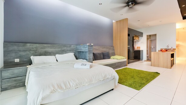 A modern bedroom with a large bed, a green rug, and a ceiling fan. - Akademik Suites (Johor Bahru)