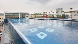 A large indoor swimming pool with a clear blue water surface, surrounded by a modern building with a covered seating area and a playground with slides. - Akademik Suites (Johor Bahru)