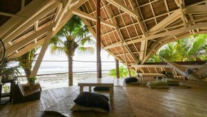 Eine Strandhütte mit einem Reetdach, Holzboden und einer Hängematte.