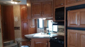 A compact RV kitchen with wooden cabinets, a black stove, a microwave, and a sink with a window above it. - Near Blue Springs Pk (Orange City)