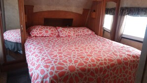 A bed with a patterned bedspread in a room with wooden headboard and a window with curtains. - Near Blue Springs Pk (Orange City)