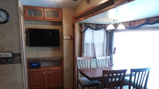 A compact kitchen with wooden cabinets, a flat-screen TV, and a dining area with a table and chairs. - Near Blue Springs Pk (Orange City)