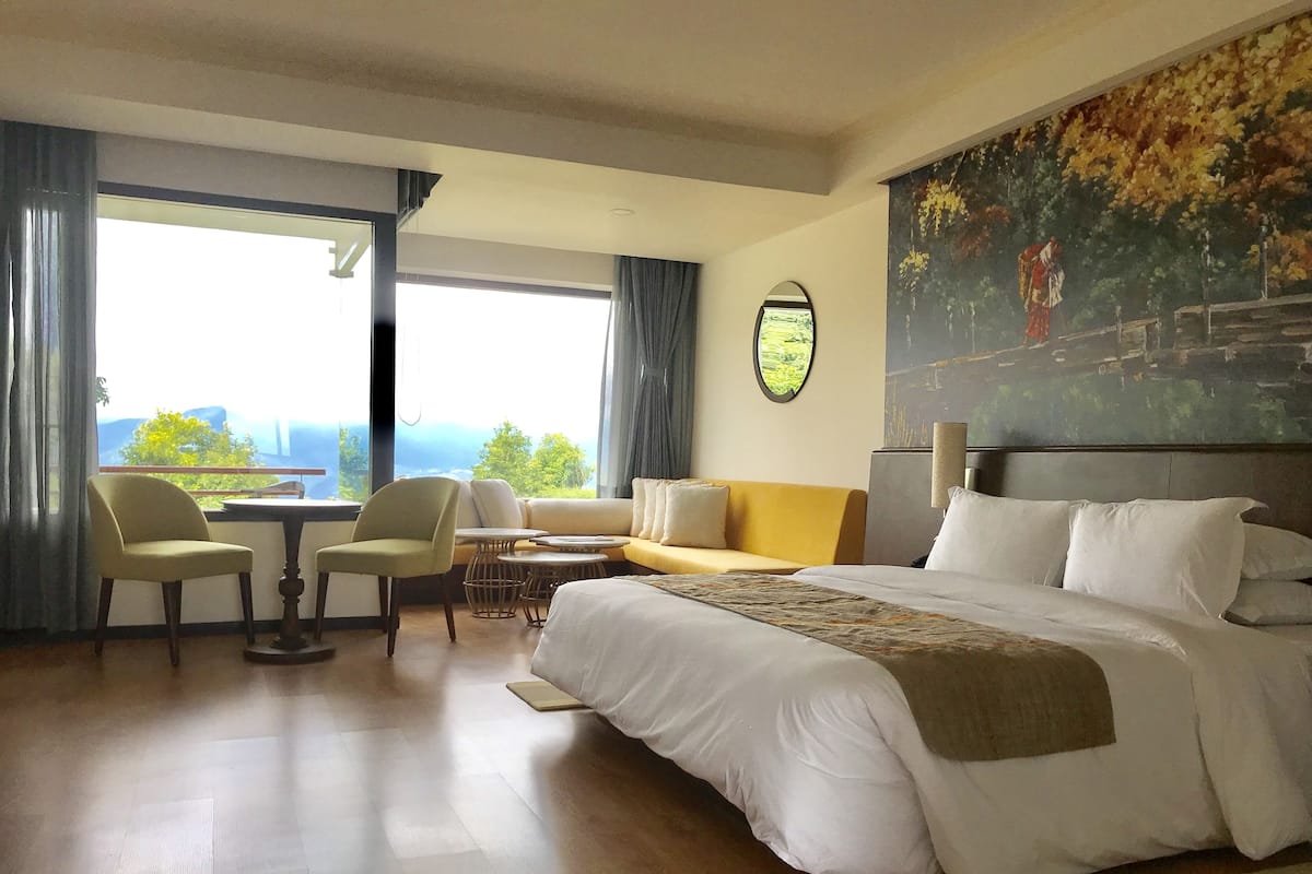 Habitació d'hotel amb un llit gran, un sofà, dues cadires, una taula petita i un quadre a la paret.