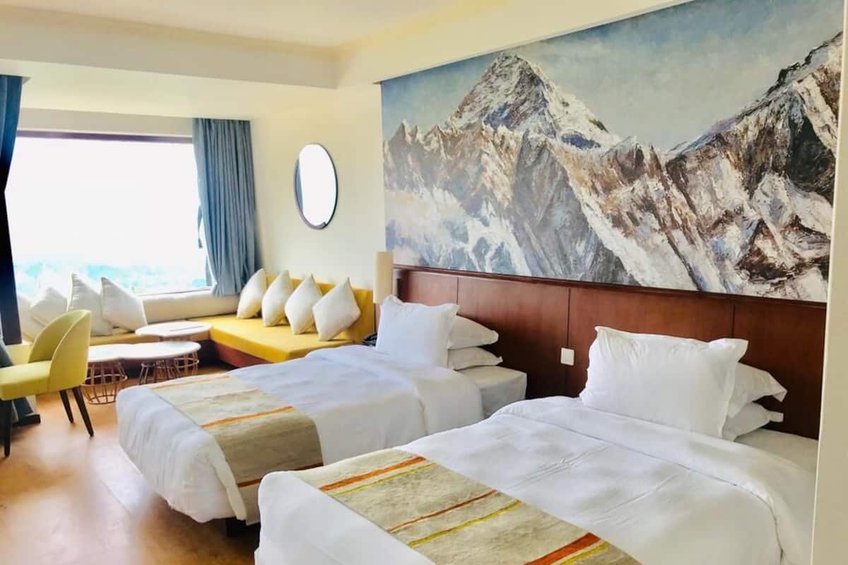 Habitació d'hotel amb dos llits, un sofà, una cadira i un quadre gran amb una muntanya a la paret.