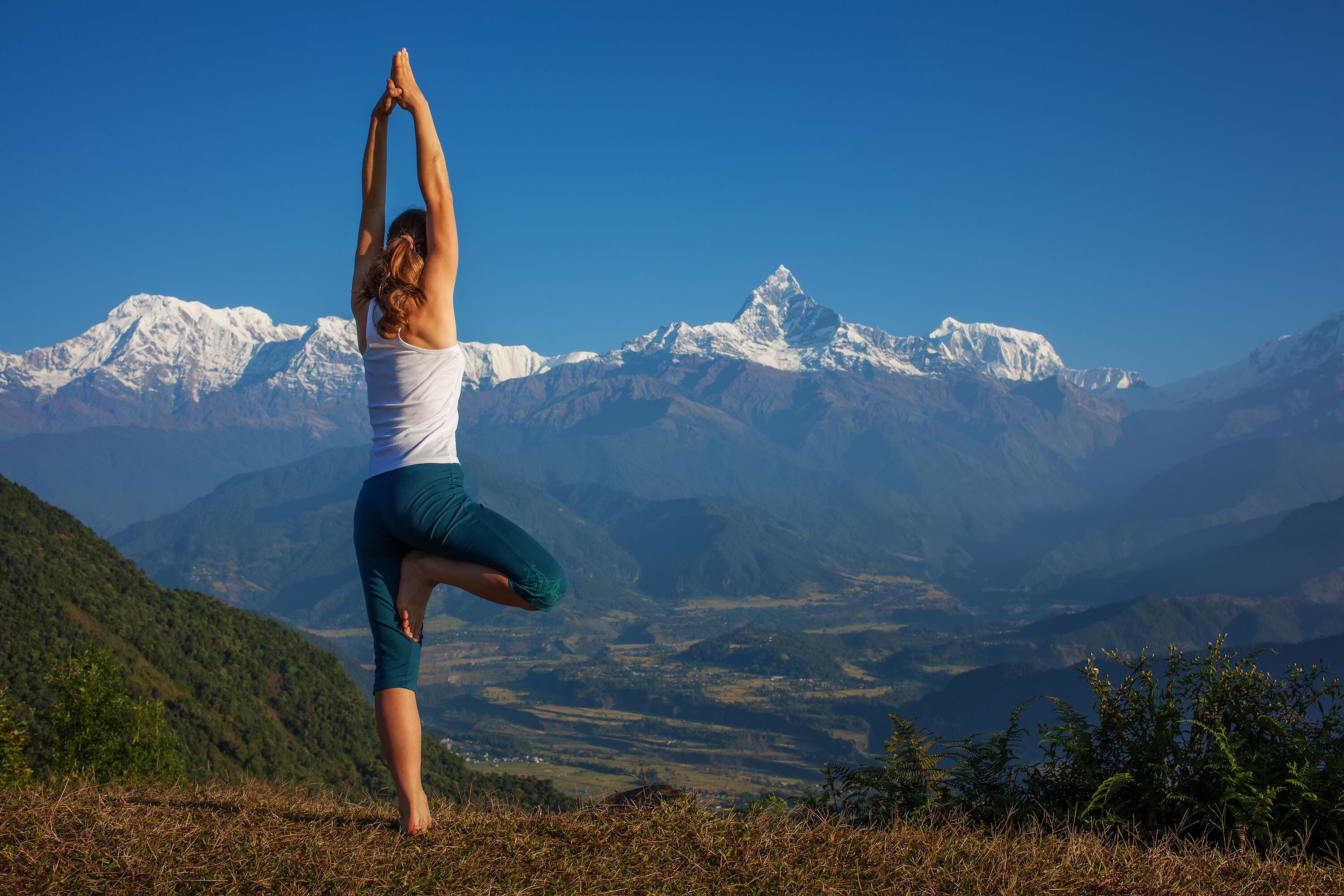 A person performing a yoga pose on a grassy hill with a mountain range in the background.