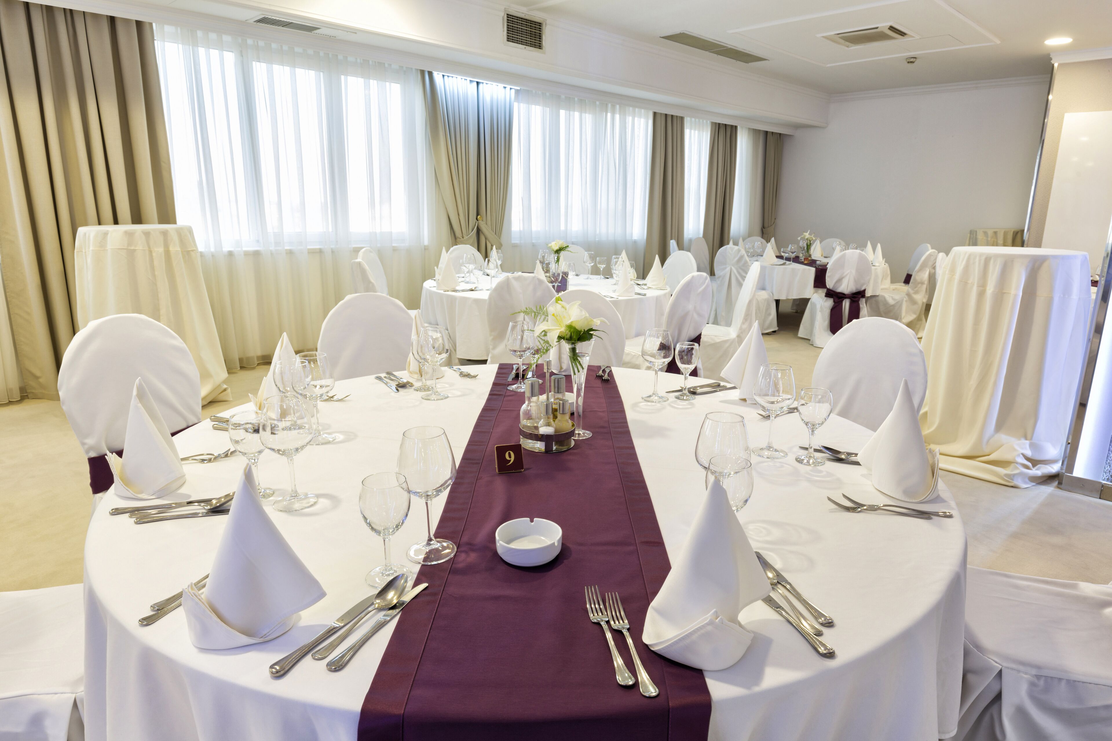 A banquet hall with round tables, white tablecloths, and white chairs.