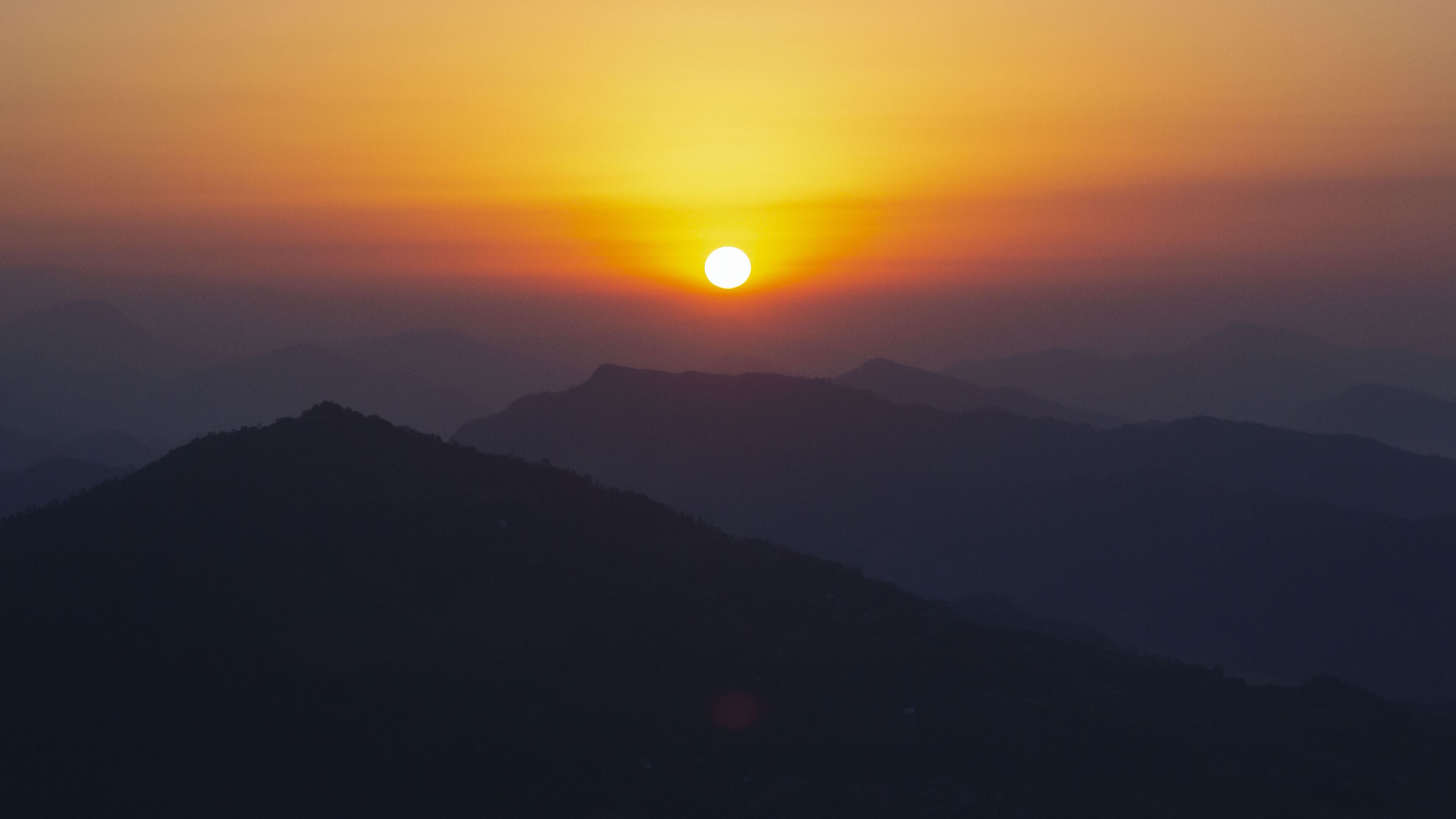 A mountain landscape during sunset with a visible sun.
