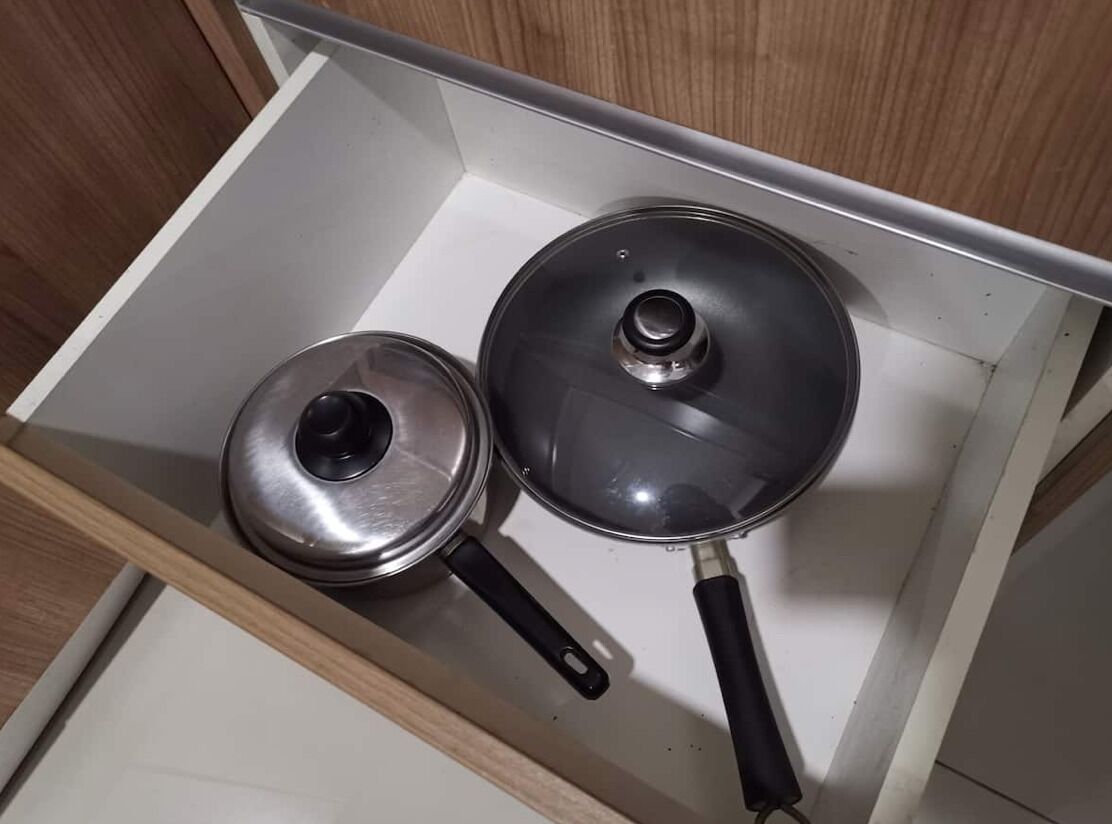 A drawer with two pots, one with a lid and one without, in a kitchen setting.