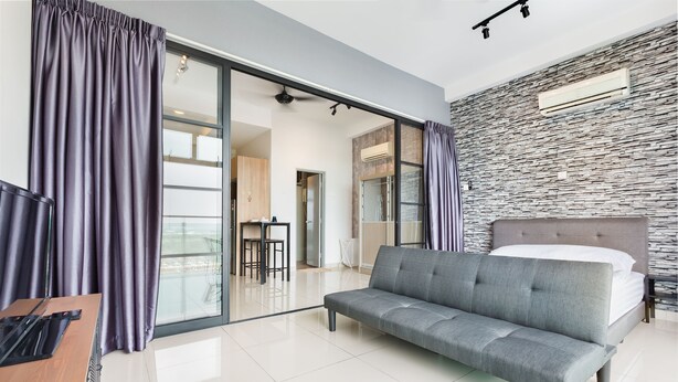 A modern hotel room with a grey sofa, a bed with white linens, and a stone-textured wall. - Palazio Serviced Apartment (Johor Bahru)