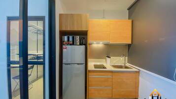 A compact kitchen with wooden cabinets, a stainless steel refrigerator, a sink, and a small countertop.