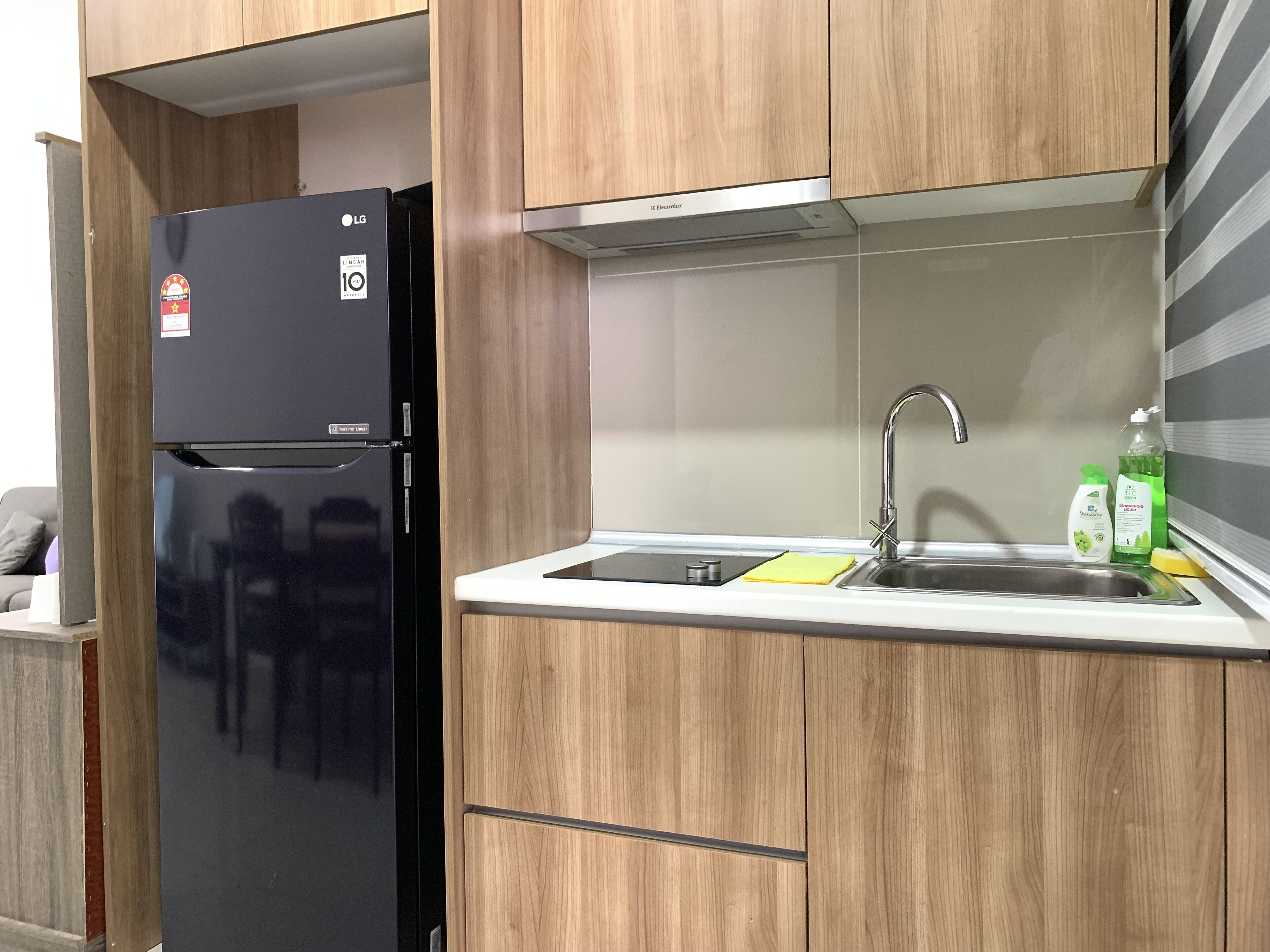 A kitchen with a black refrigerator, wooden cabinets, a stainless steel sink, and a countertop.