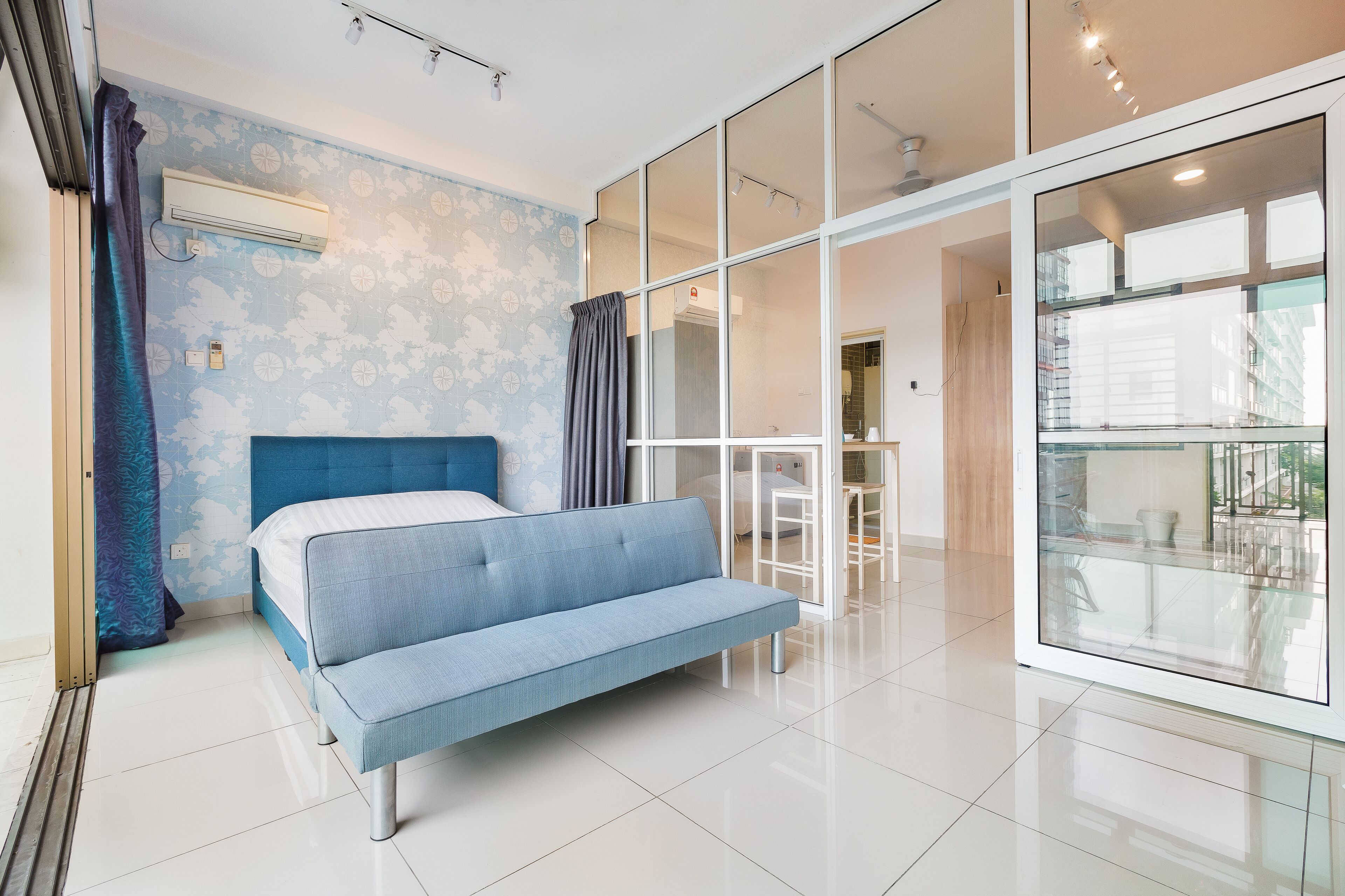 Een moderne kamer met een blauwe bank, een groot raam en een glazen scheidingswand.