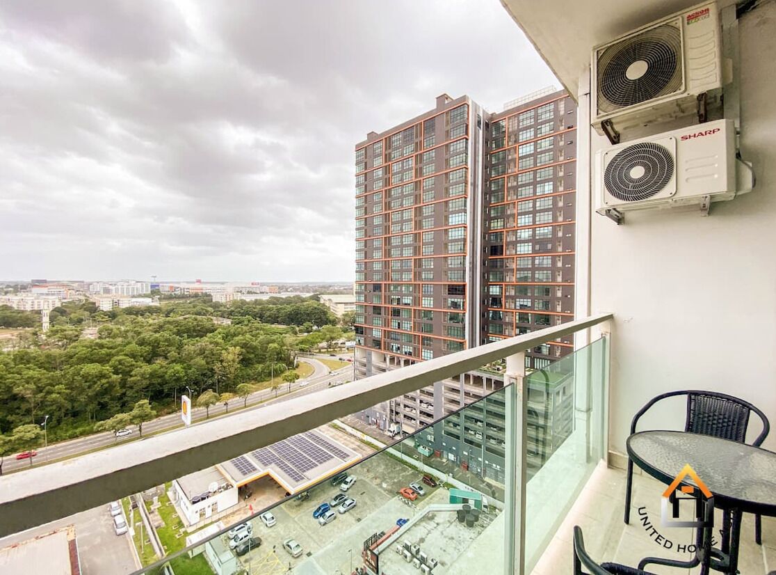 A high-rise building with multiple floors, air conditioning units on the wall, a balcony with a glass railing, and a view of a parking lot and greenery below.