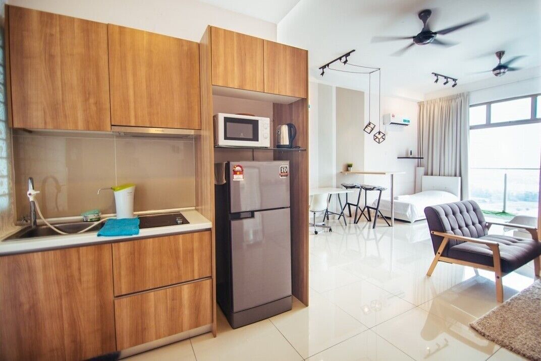 A modern kitchen with wooden cabinets, a microwave, and a refrigerator. There is a dining area with a table and chairs, and a large window providing natural light.
