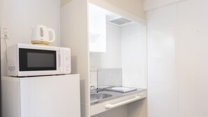 A compact kitchen with a white refrigerator, microwave, and kettle. - Hotel Houklea (Nago)