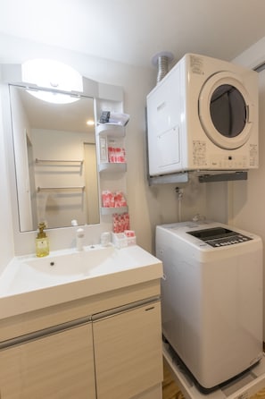 A bathroom with a white sink, mirror, and a built-in washing machine. - Hotel Houklea (Nago)