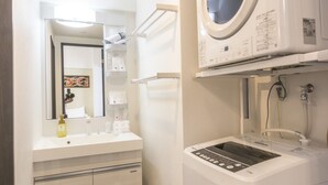 A compact bathroom with a white sink, mirror, and a stacked washer and dryer unit. - Hotel Houklea (Nago)