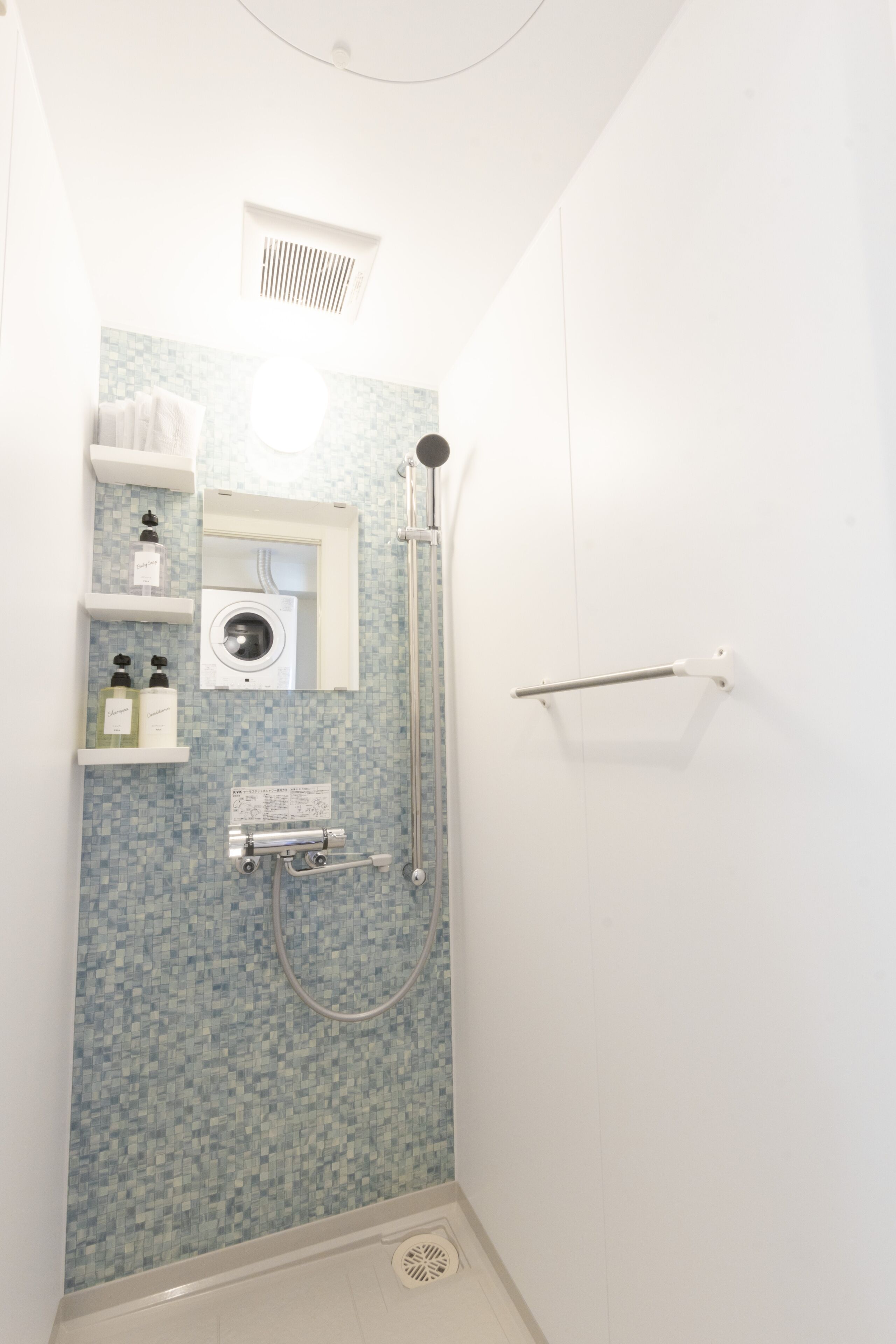 A small, narrow bathroom with a shower, a built-in washing machine, and a towel rack.