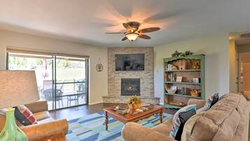 A living room with a fireplace, a ceiling fan, a sofa, a coffee table, and a bookshelf.