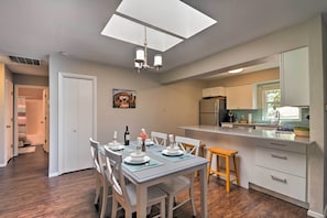 A modern kitchen with white cabinetry, a dining area with a table set for four, and a skylight above.