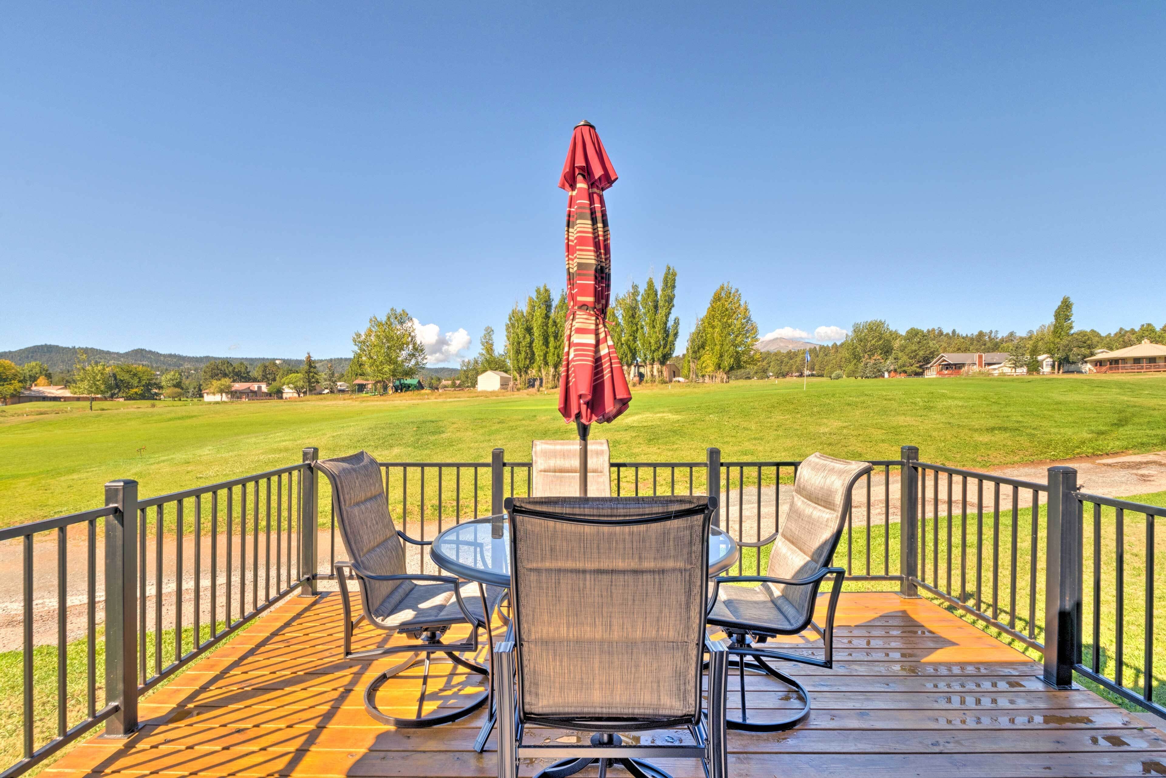 A deck with a table and chairs, a red umbrella, and a view of a grassy field and trees.