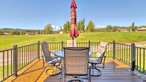 A deck with a table and chairs, a red umbrella, and a view of a grassy field and trees.