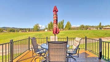 A deck with a table and chairs, a red umbrella, and a view of a grassy field and trees.