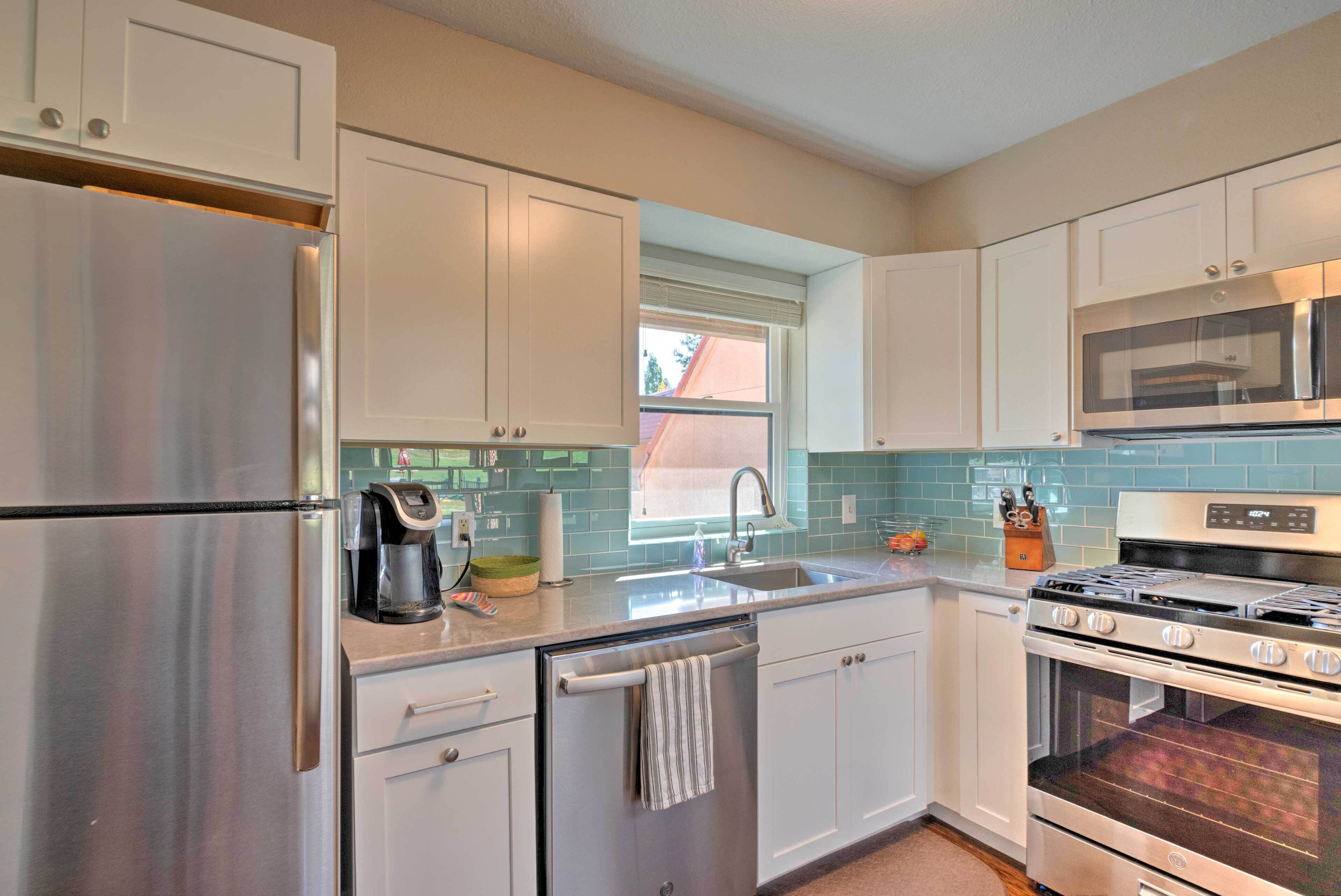 A modern kitchen with white cabinets, stainless steel appliances, a dishwasher, and a window with a view.