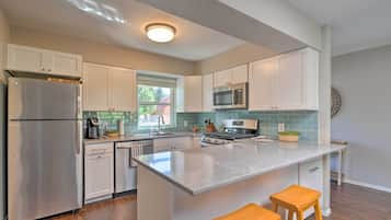 A modern kitchen with white cabinets, stainless steel appliances, a large island with stools, and a window providing natural light.
