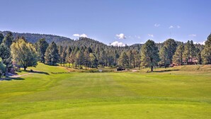 A golf course with a clear view of the green, trees, and distant hills.