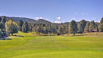 A golf course with a clear view of the green, trees, and distant hills.