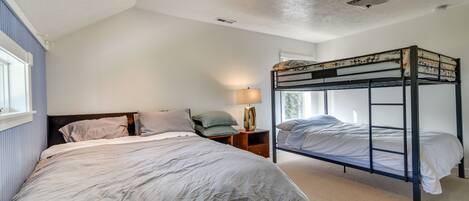 A bedroom with a single bed, a bunk bed, a nightstand with a lamp, and a window with blinds.