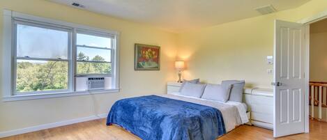 A bedroom with a large window, a bed with a blue blanket, a bedside lamp, and a door to another room.