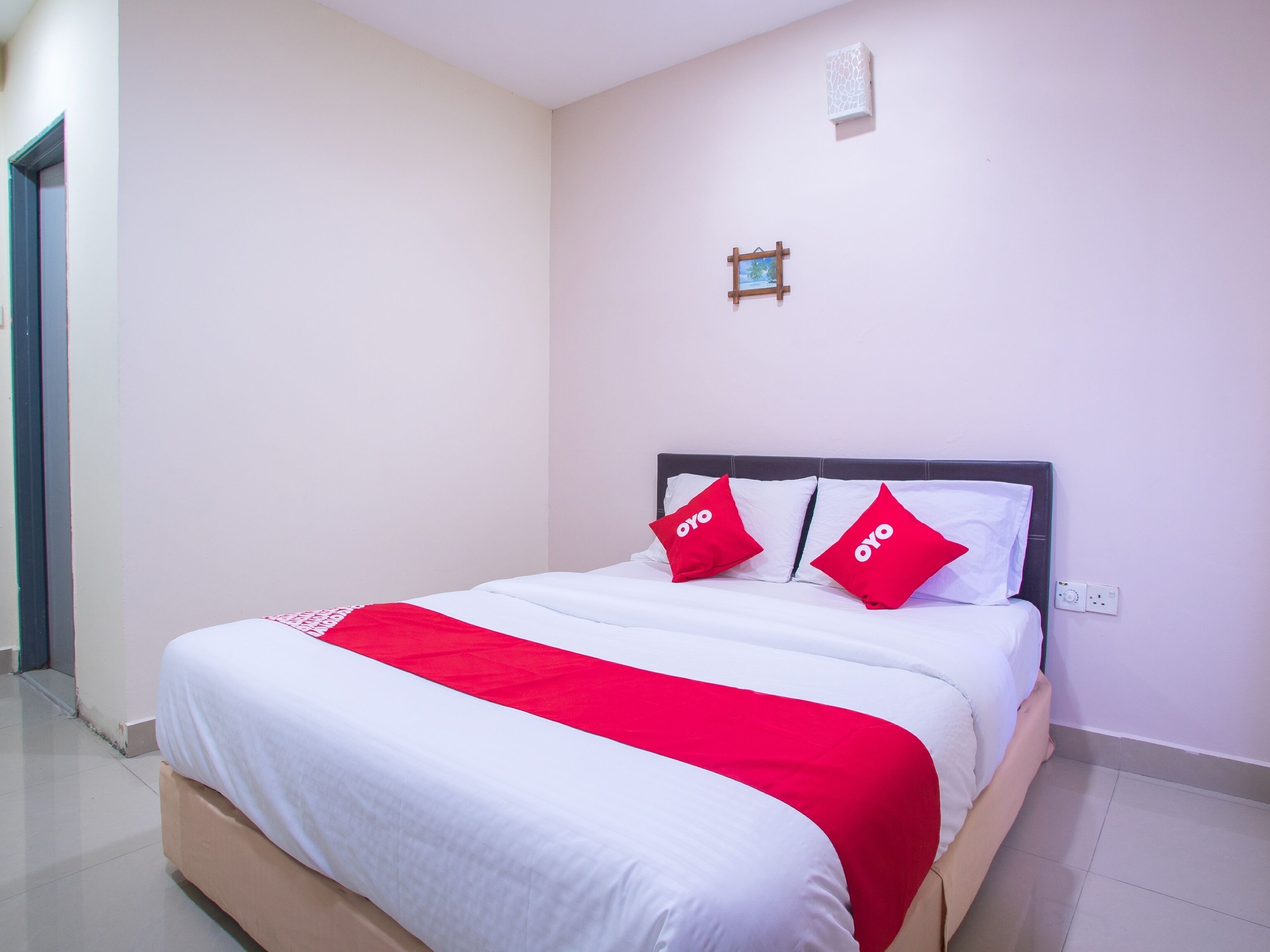 Una cama bien hecha con ropa de cama blanca y roja, un aire acondicionado pequeño montado en la pared y un enchufe en la pared.