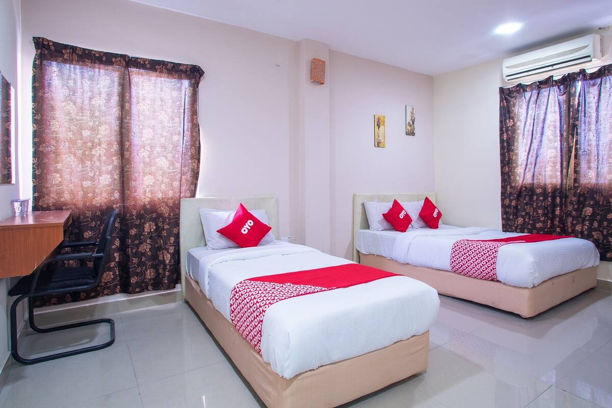 A hotel room with two beds, a desk, and an air conditioning unit.