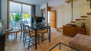 A modern living room with a glass dining table, comfortable seating, a TV, and a staircase leading to another level. - Vacation home Golf by Interhome (Can Picafort)