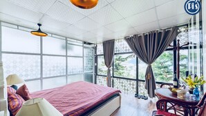 A hotel room with a bed, a table with chairs, a window with curtains, and a view of greenery outside. - Pi's Boutique Hotel (Sa Pa)