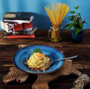 A plate of spaghetti with a garnish, a fork, and a glass jar of pasta on a wooden table. - Pi's Boutique Hotel (Sa Pa)