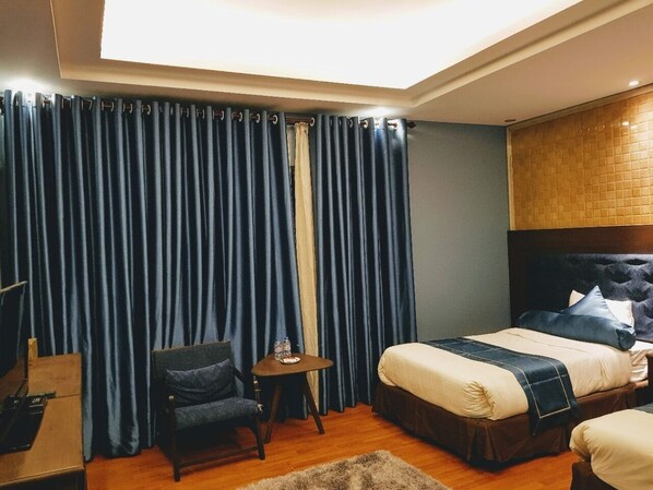 A hotel room with a bed, a chair, a small table, and a curtain.