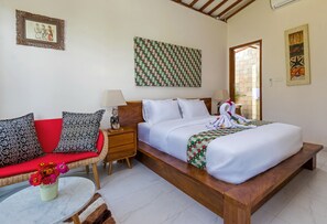 A bedroom with a bed, a nightstand, a red sofa, and a small table with flowers. - Villa Ronggo Mayang Bali (Selemadeg)