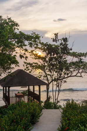A gazebo with a tiled roof and a bench, surrounded by lush greenery and a view of the sea. - Villa Ronggo Mayang Bali (Selemadeg)