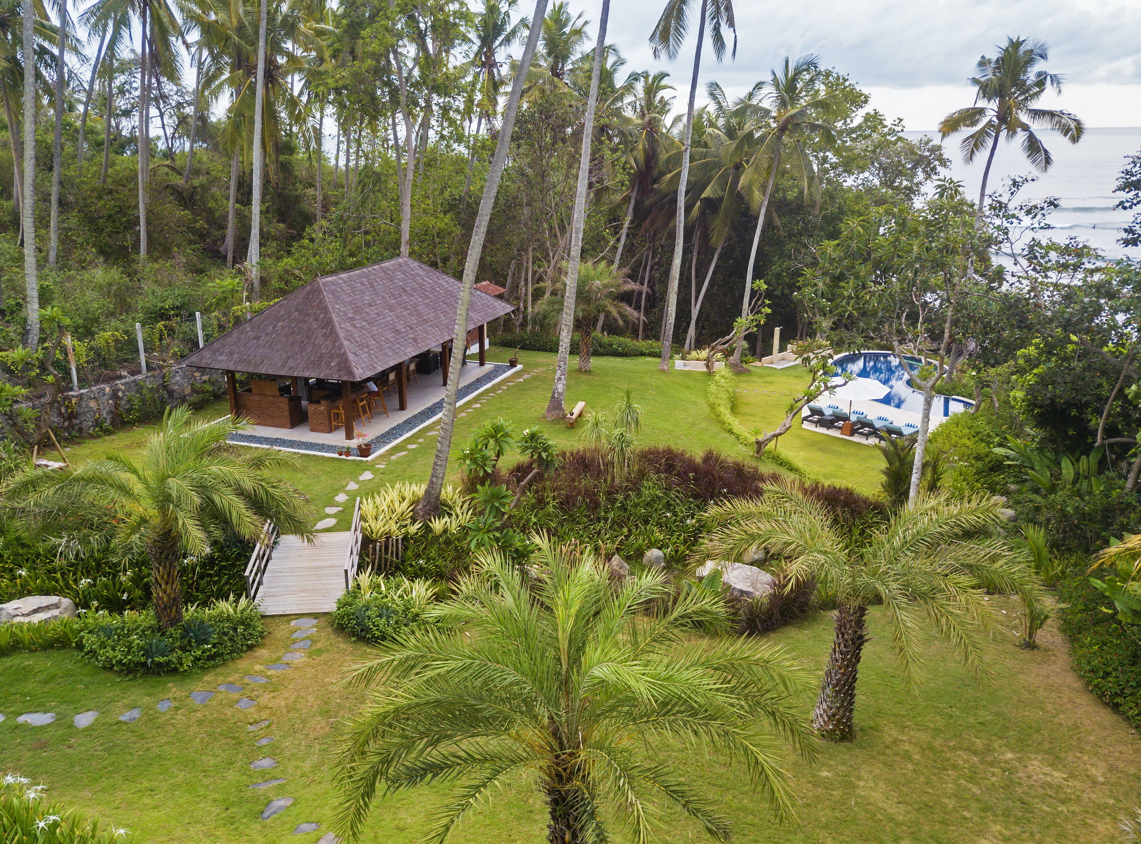 A tropical resort with a thatched-roof hut, a pool, and lush greenery.