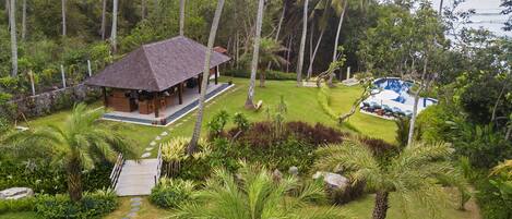 A tropical resort with a thatched-roof hut, a pool, and lush greenery.