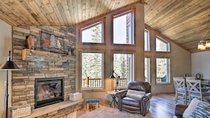 A cozy living room with a stone fireplace, large windows, and a leather chair. - Fairplay Cabin w/ Wraparound Deck & Mountain Views (Fairplay)