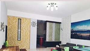 Una sala de estar moderna con una mesa de madera, cojines coloridos, un sofá grande y un televisor de pared que muestra 'Atlantico'.